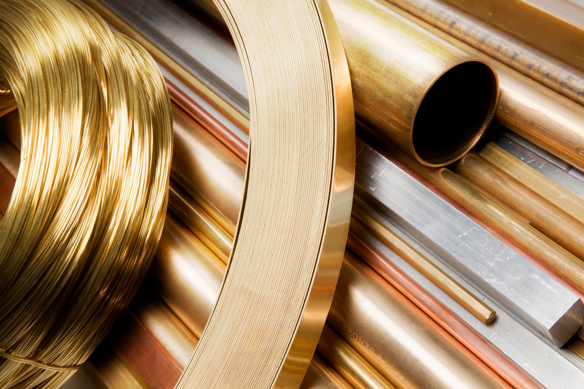 Gold wire coils, brass strip and copper tubing representing precious-metal mill products