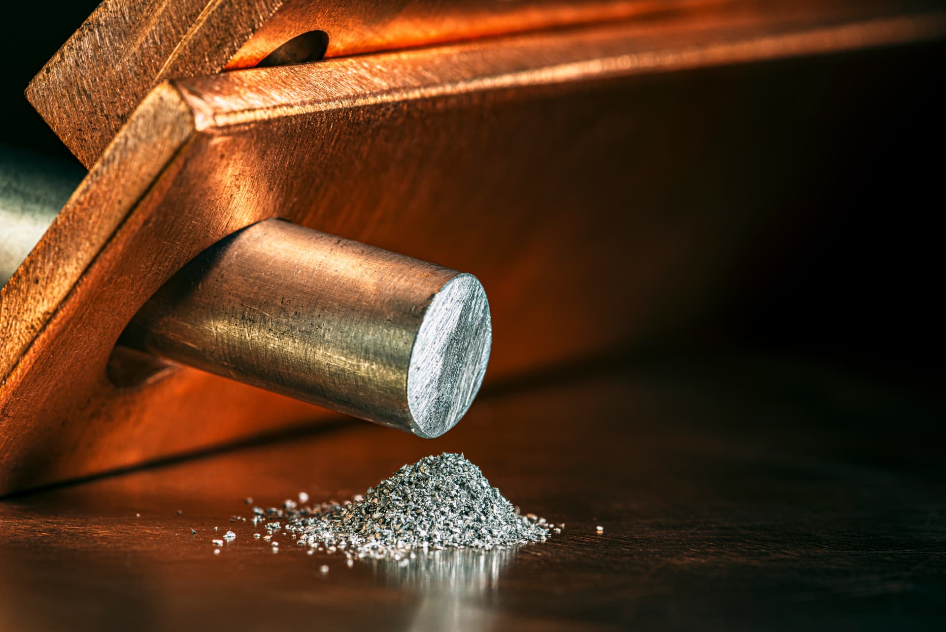 A machined metal rod protruding from a copper block above a pile of metal shavings