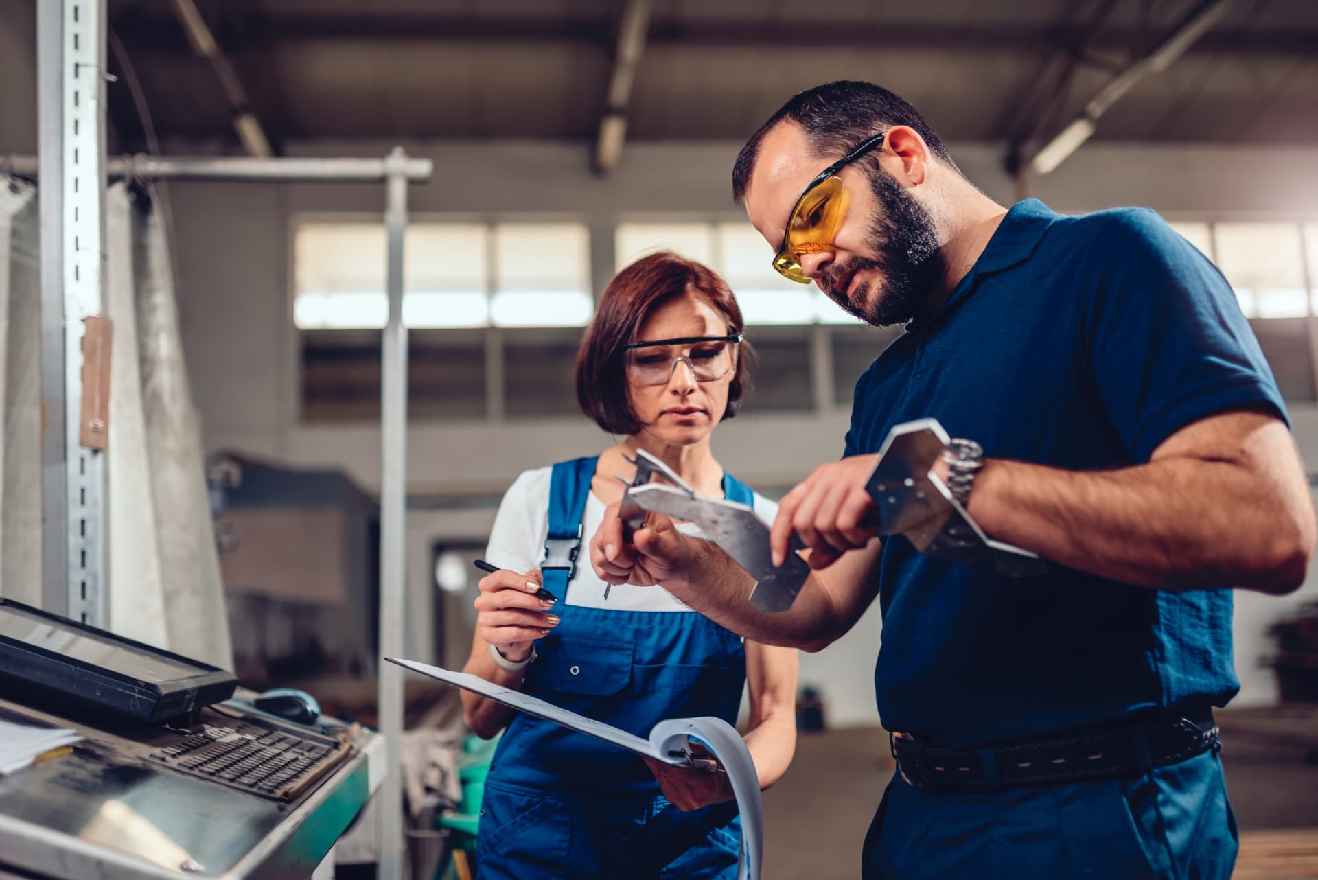 Two manufacturing specialists inspecting a machined metal component on the factory floor